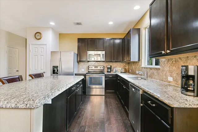 a large kitchen with granite countertop a sink counter space stainless steel appliances and cabinets
