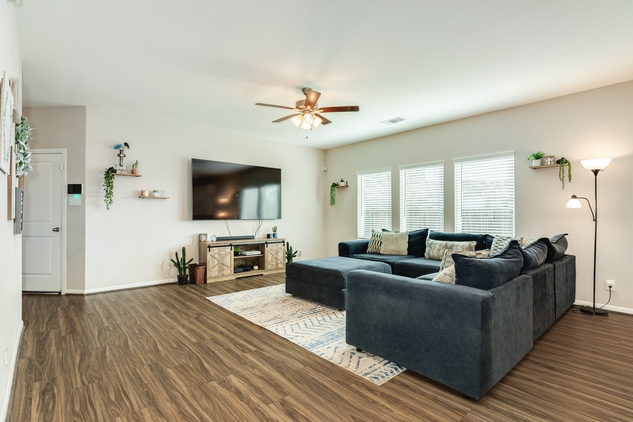2446 Palisade Crst Drive Rosharon, TX 77583 - Photo 6 of 30 Spacious living room with wood like flooring, featuring room for a large sectional sofa, ceiling fan, and ample natural light from three windows. The room includes a wall-mounted TV, modern decor, and a cozy atmosphere.