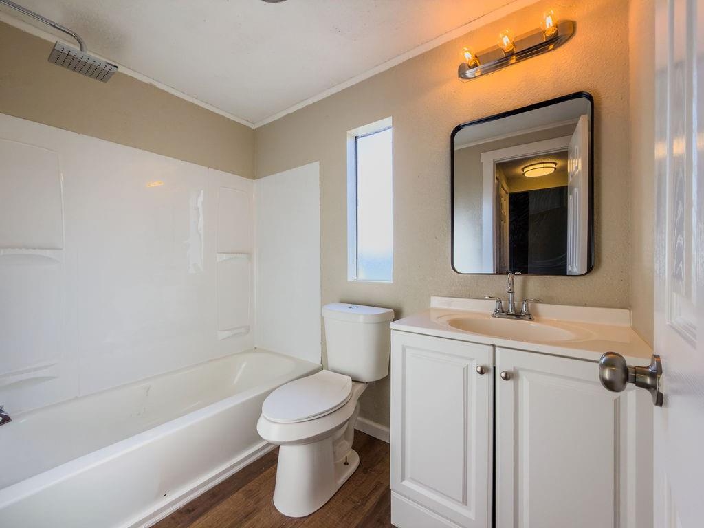 109 Brookshire Street Riesel, TX 76682 - Photo 13 of 18 Bathroom featuring a tub/shower combination with a square rainfall showerhead, a white vanity with panel doors and silver-tone hardware, a rectangular mirror, and wood-finish flooring