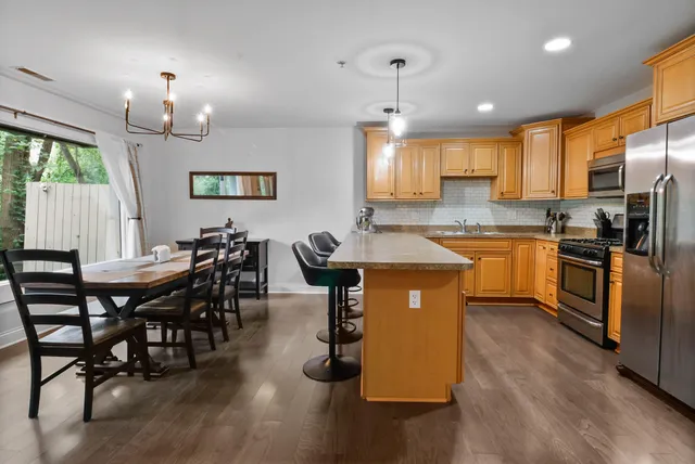 a kitchen with stainless steel appliances granite countertop a stove a sink a microwave a dining table and chairs with wooden floor