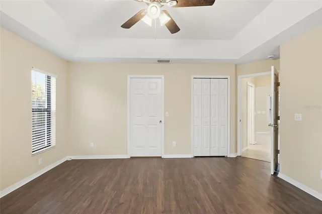 an empty room with wooden floor chandelier fan and windows