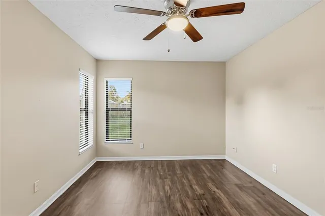 an empty room with wooden floor ceiling fan and windows