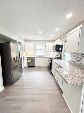 a large white kitchen with a stove a sink dishwasher a refrigerator and white cabinets with wooden floor