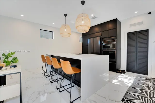 a kitchen with stainless steel appliances kitchen island granite countertop a refrigerator a stove a microwave oven a large island with chairs and wooden floor