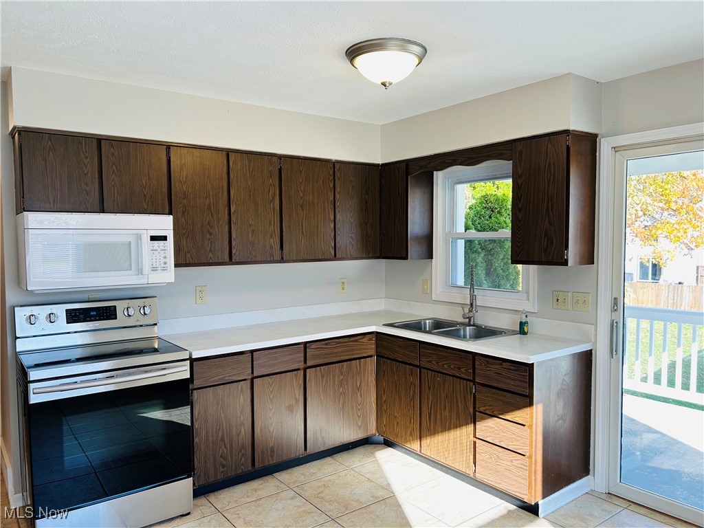 522 State Road Northwest Warren, OH 44483 - Photo 7 of 29 Kitchen with stainless steel range with electric cooktop, dark brown cabinetry, white microwave, light countertops, and light tile patterned flooring