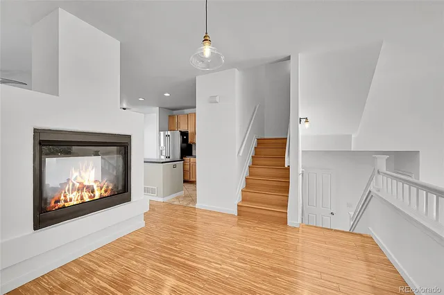 a view of an empty room with wooden floor fire place and a kitchen