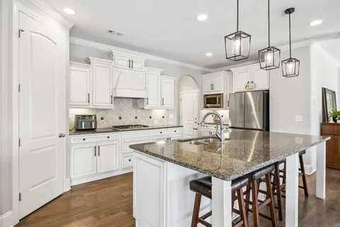 a kitchen with stainless steel appliances granite countertop a sink a stove a refrigerator and island with wooden floor