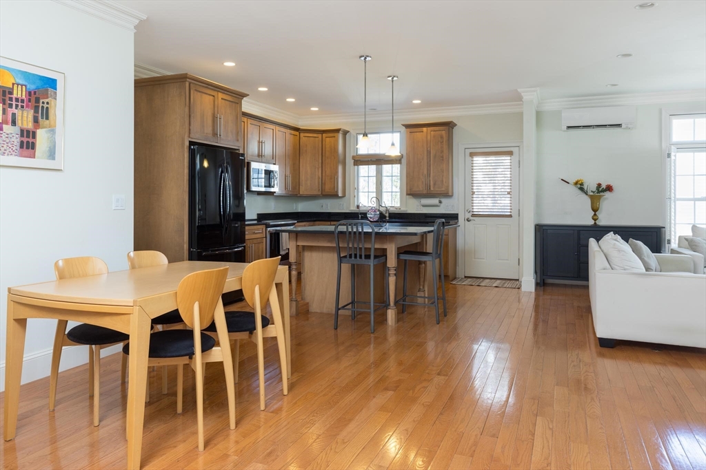 38 Maple Street, Unit 38 Needham, MA 02492 - Photo 3 of 14 a kitchen with stainless steel appliances granite countertop a stove a refrigerator a kitchen island a dining table and chairs with wooden floor