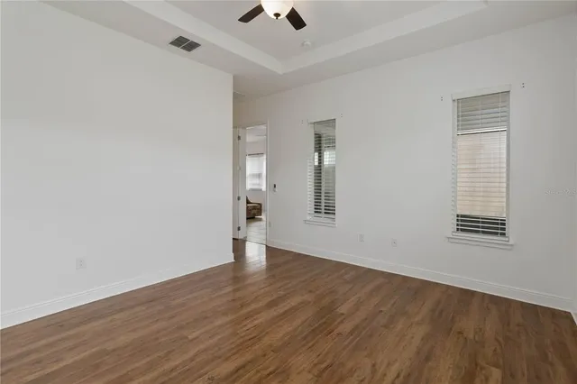 an empty room with wooden floor chandelier fan and windows