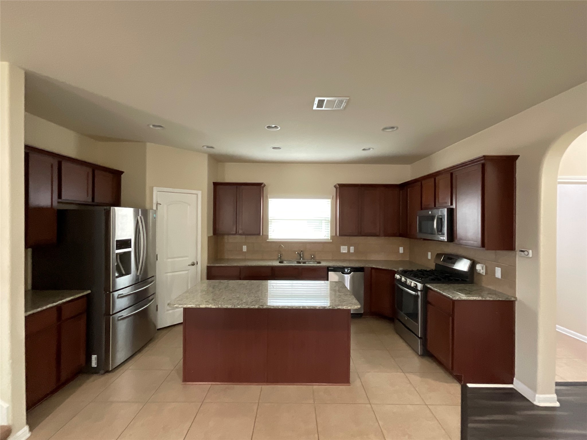 3451 Mayfield Ranch Boulevard, Unit 311 Round Rock, TX 78681 - Photo 8 of 29 Kitchen featuring stainless steel appliances, arched walkways, light stone countertops, backsplash, and a kitchen island