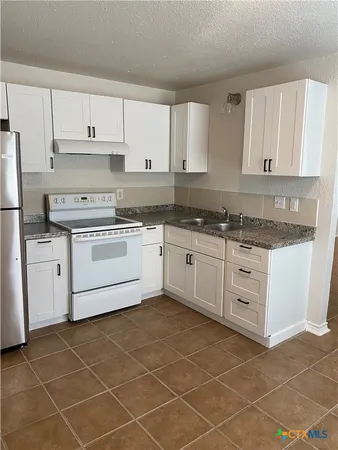 a kitchen with a stove a sink and white cabinets