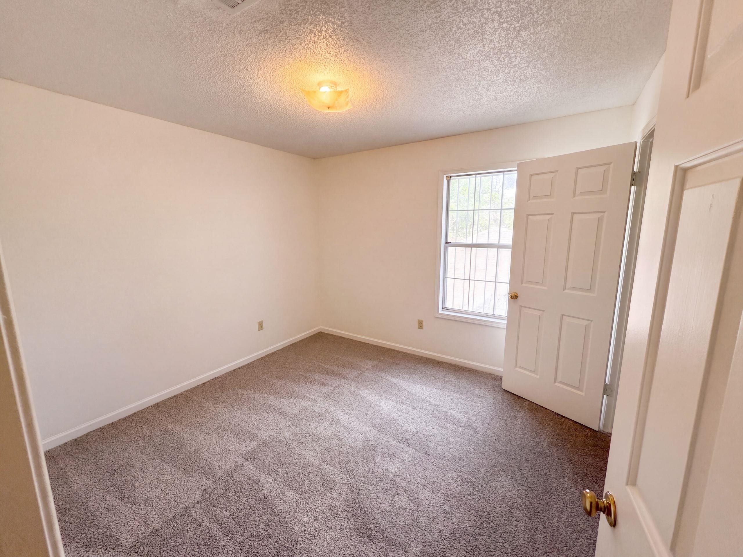 3798 Fern Ridge Road Memphis, TN 38115 - Photo 10 of 16 Neutral tone wall paint, textured ceiling, flush mount ceiling light fixture, paneled interior door, and window with security bars