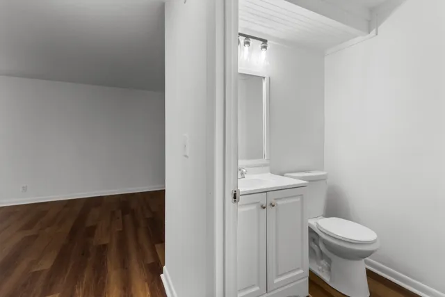 a bathroom with a toilet a sink and wooden floor
