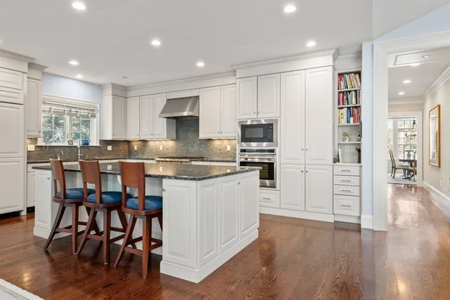 a kitchen with stainless steel appliances granite countertop a stove top oven a sink a refrigerator with white cabinets and wooden floor