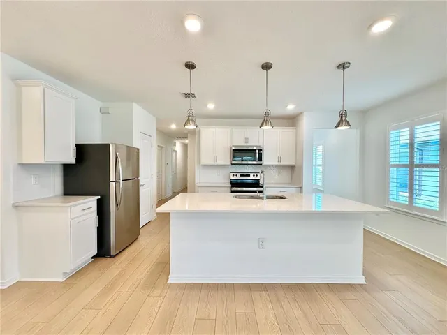 a large kitchen with stainless steel appliances a refrigerator a stove a sink dishwasher a oven and a dining table with wooden floor