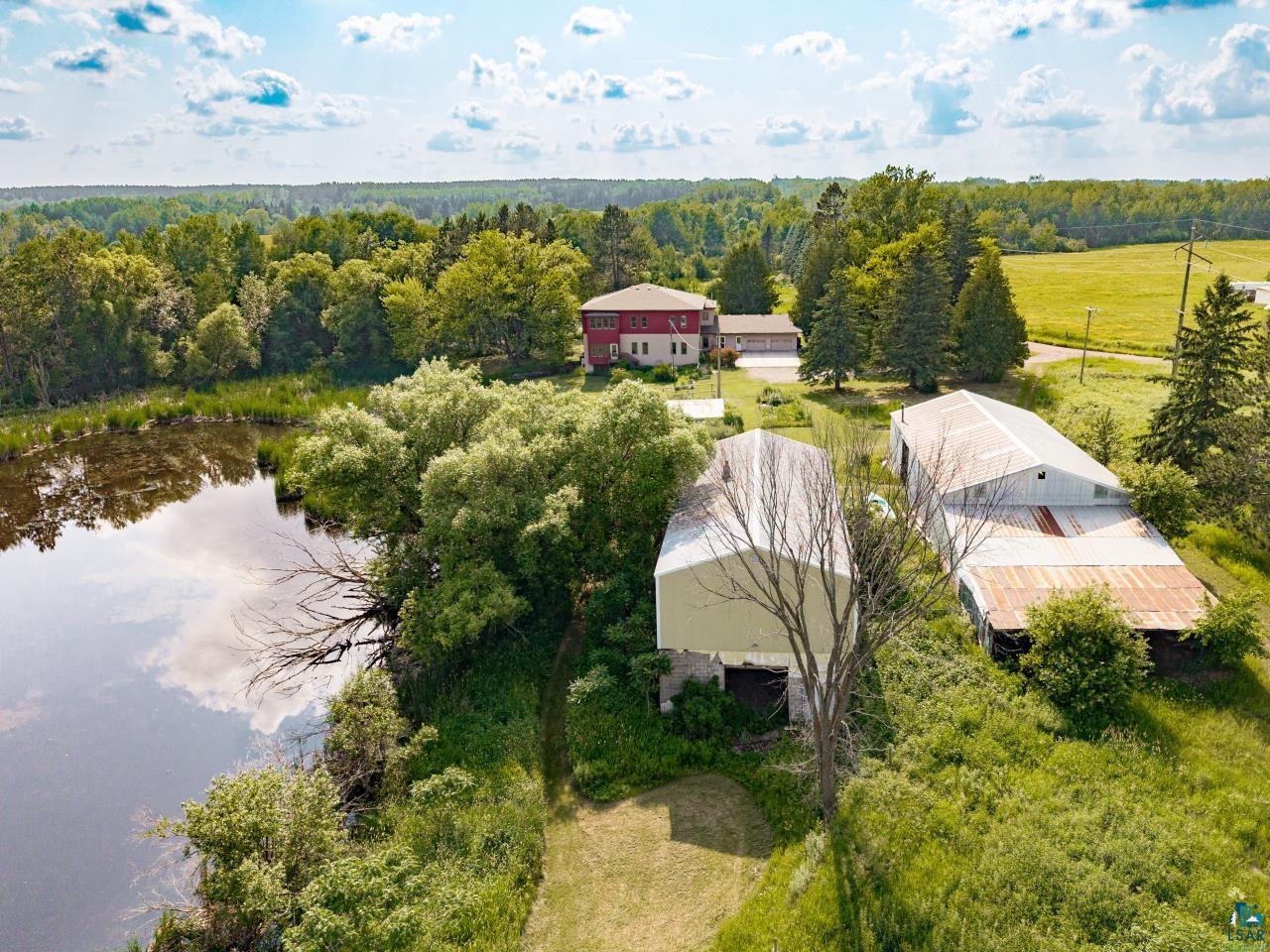 4800 Tower Road Moose Lake, MN 55767 - Photo 33 of 83 Rural property featuring a red residential building, two large outbuildings with metal roofs, and a natural pond