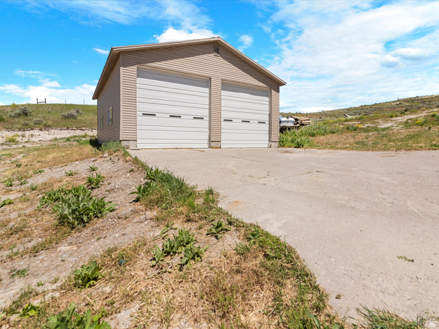 15680 North Beaver Dam Road Collinston, UT 84306 - Photo 38 of 49 Detached two-car garage with beige vinyl siding and white garage doors, set on a concrete pad with a sloped concrete drive