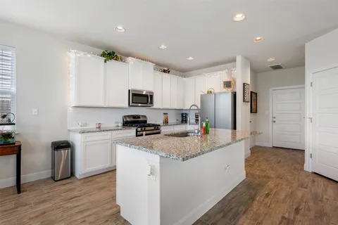 a large kitchen with stainless steel appliances granite countertop a refrigerator a sink dishwasher a oven with white cabinets and wooden floor