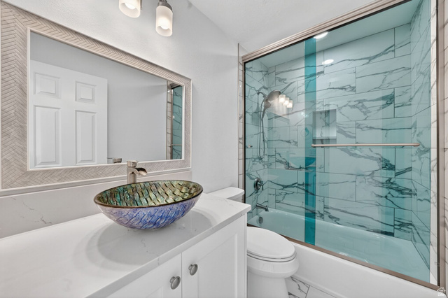 6969 South 855 East Midvale, UT 84047 - Photo 9 of 55 Bathroom featuring a vessel sink, white vanity with cabinet storage, a framed mirror, and a shower-tub combination with tile surround and glass enclosure