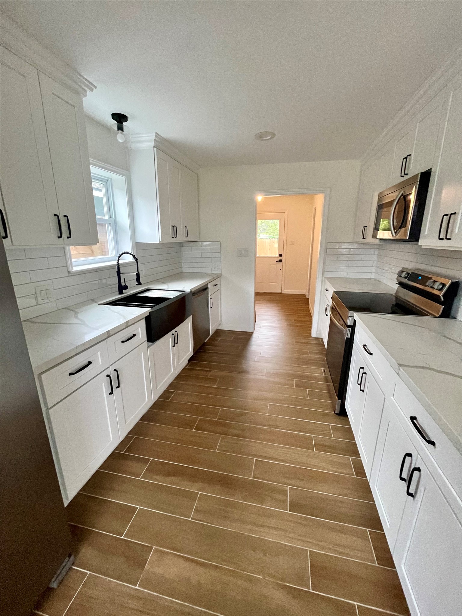 302 Moody Street Houston, TX 77009 - Photo 5 of 11 Offering a Modern kitchen with sleek white cabinets, stainless steel appliances, and a farmhouse sink. It features wood-look tile flooring and bright, spacious countertops. Ideal for cooking enthusiasts.