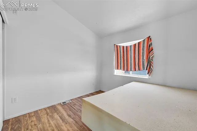 a view of an empty room with wooden floor and a window