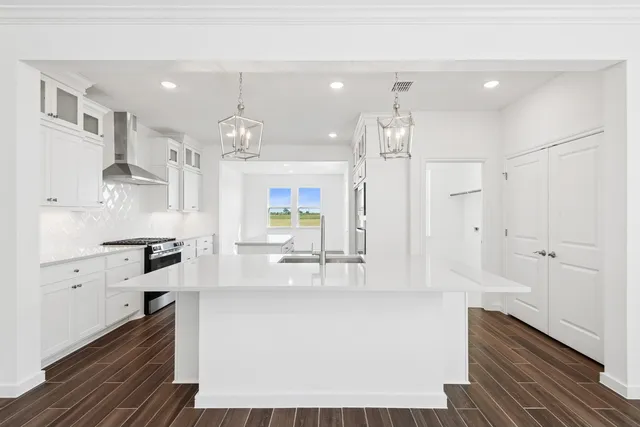 a large white kitchen with kitchen island a stove a sink dishwasher and white cabinets with wooden floor