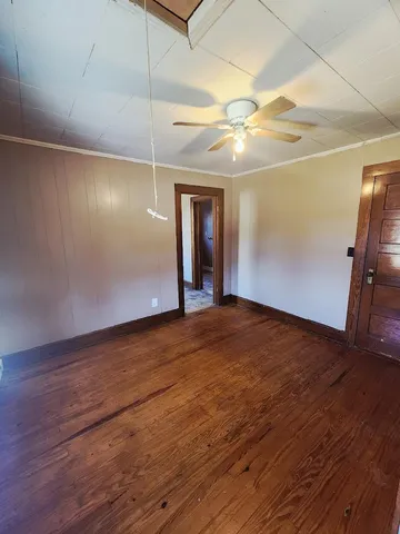 a view of an empty room with wooden floor and a ceiling fan