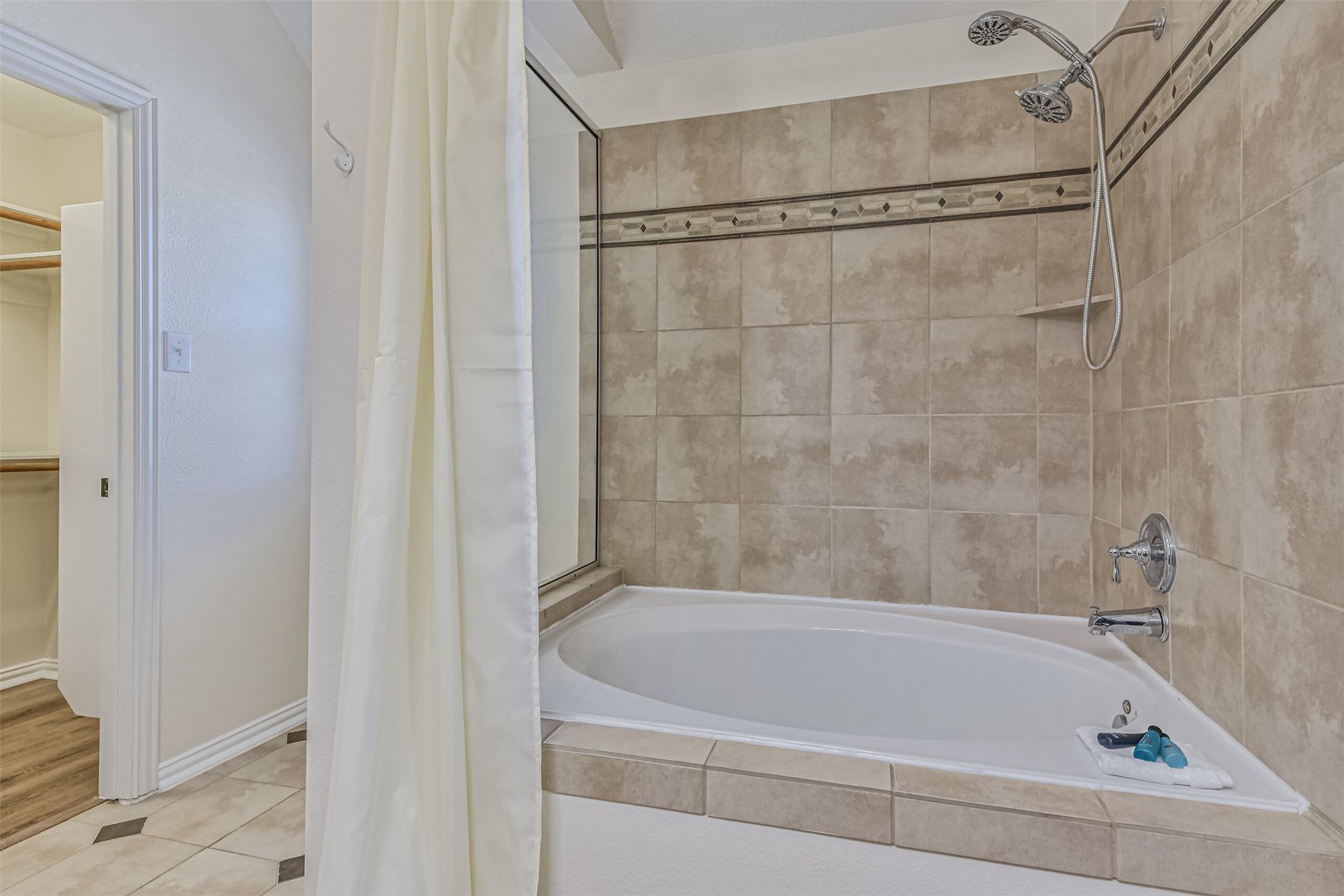 1815 28th Street Galveston, TX 77550 - Photo 16 of 42 This bathroom features a spacious bathtub with a tile surround and a dual showerhead. It connects to a walk-in closet, offering convenient access.