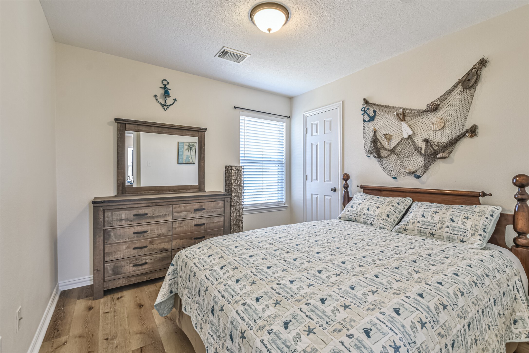 1815 28th Street Galveston, TX 77550 - Photo 17 of 42 Cozy bedroom with nautical decor, featuring a wooden dresser, a bed with themed bedding, and wall accents like an anchor and netting. The room has natural light from a window and a small closet.
