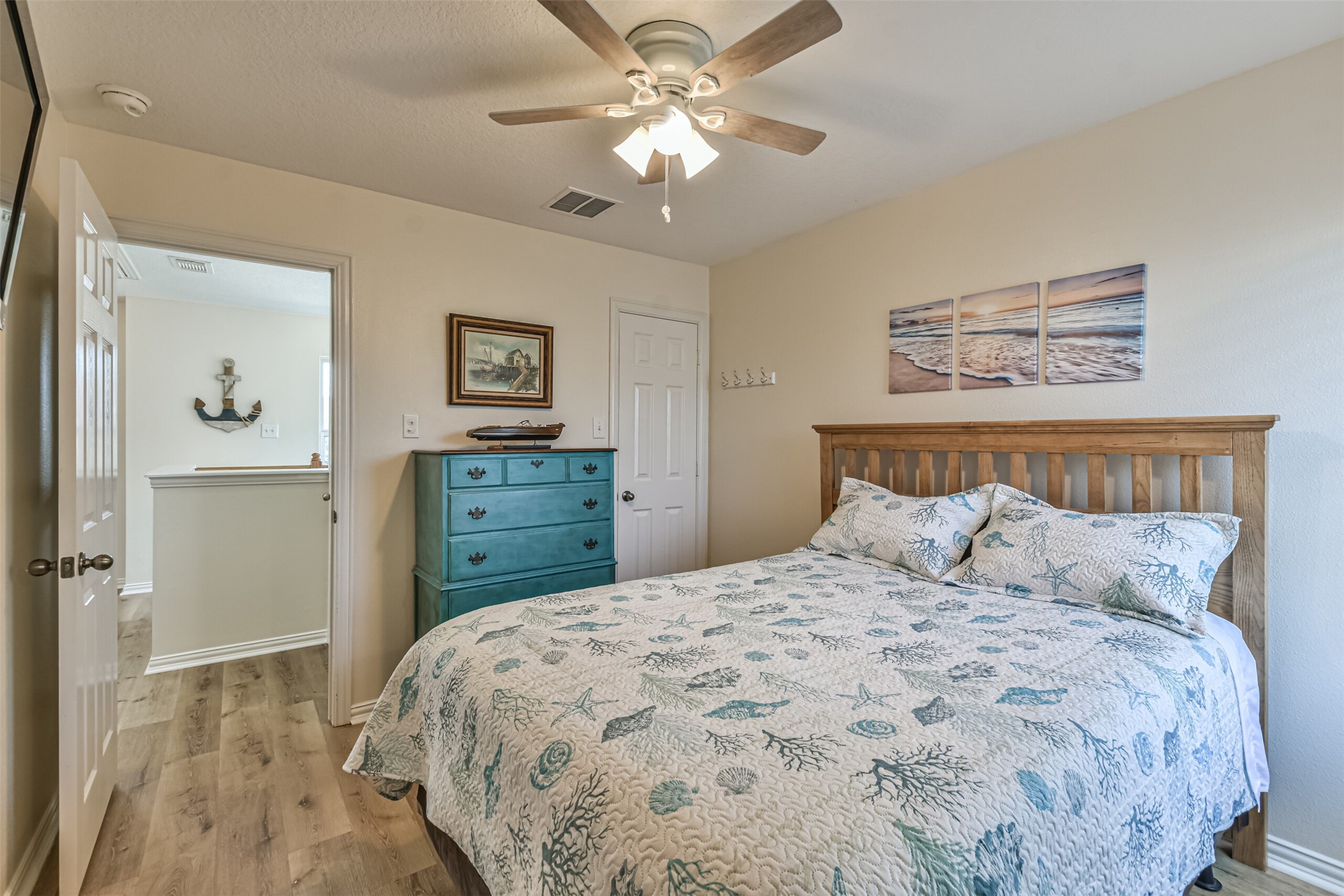 1815 28th Street Galveston, TX 77550 - Photo 20 of 42 Cozy bedroom with a beachy theme, featuring a wooden bed frame, ocean-inspired bedding, and a turquoise dresser. Ceiling fan and soft lighting create a relaxed atmosphere.