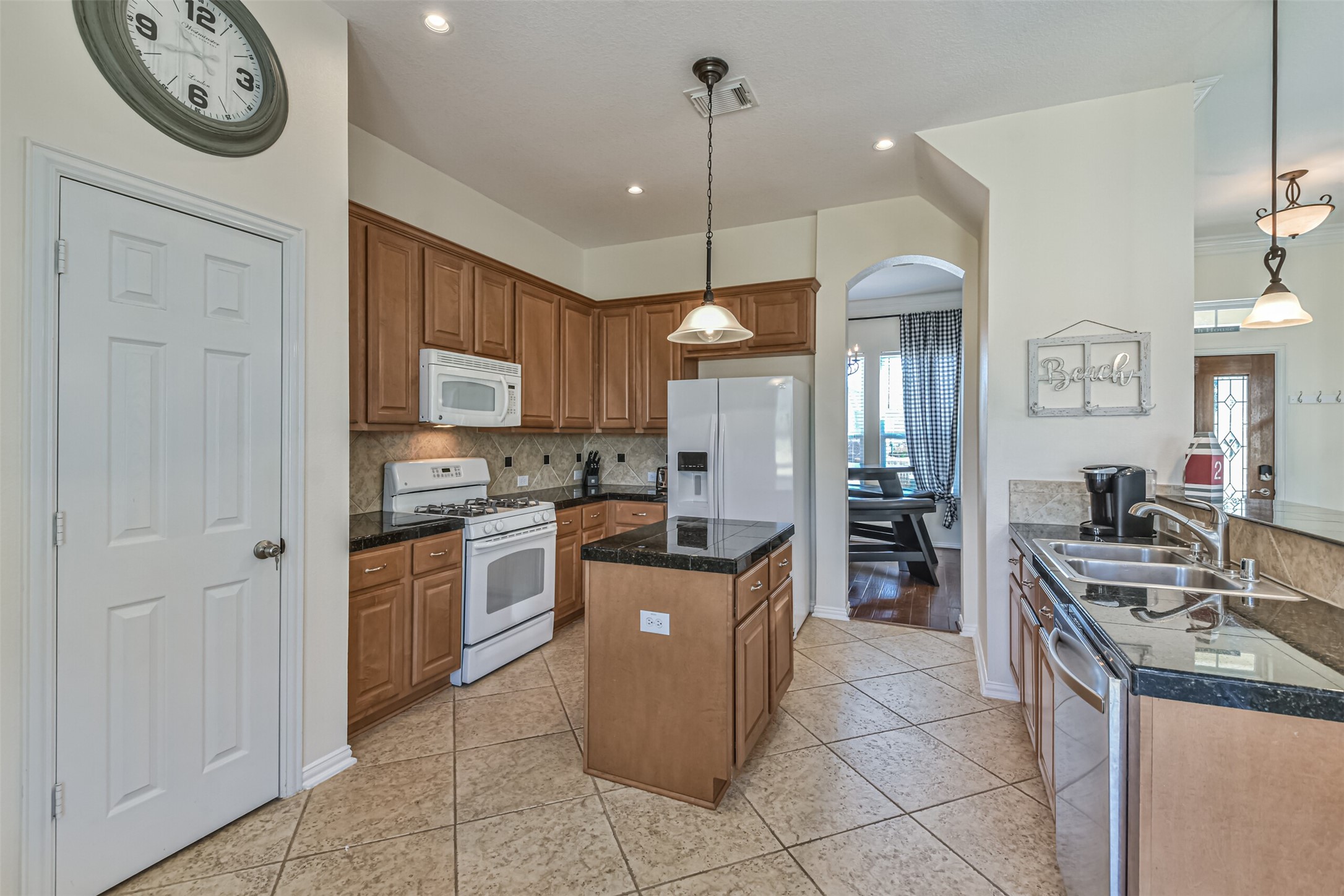 1815 28th Street Galveston, TX 77550 - Photo 27 of 42 A bright kitchen with tiled floors, featuring wooden cabinets and granite countertops. It includes modern appliances, a central island, and pendant lighting, providing a cozy and functional space. An open archway leads to the dining area.