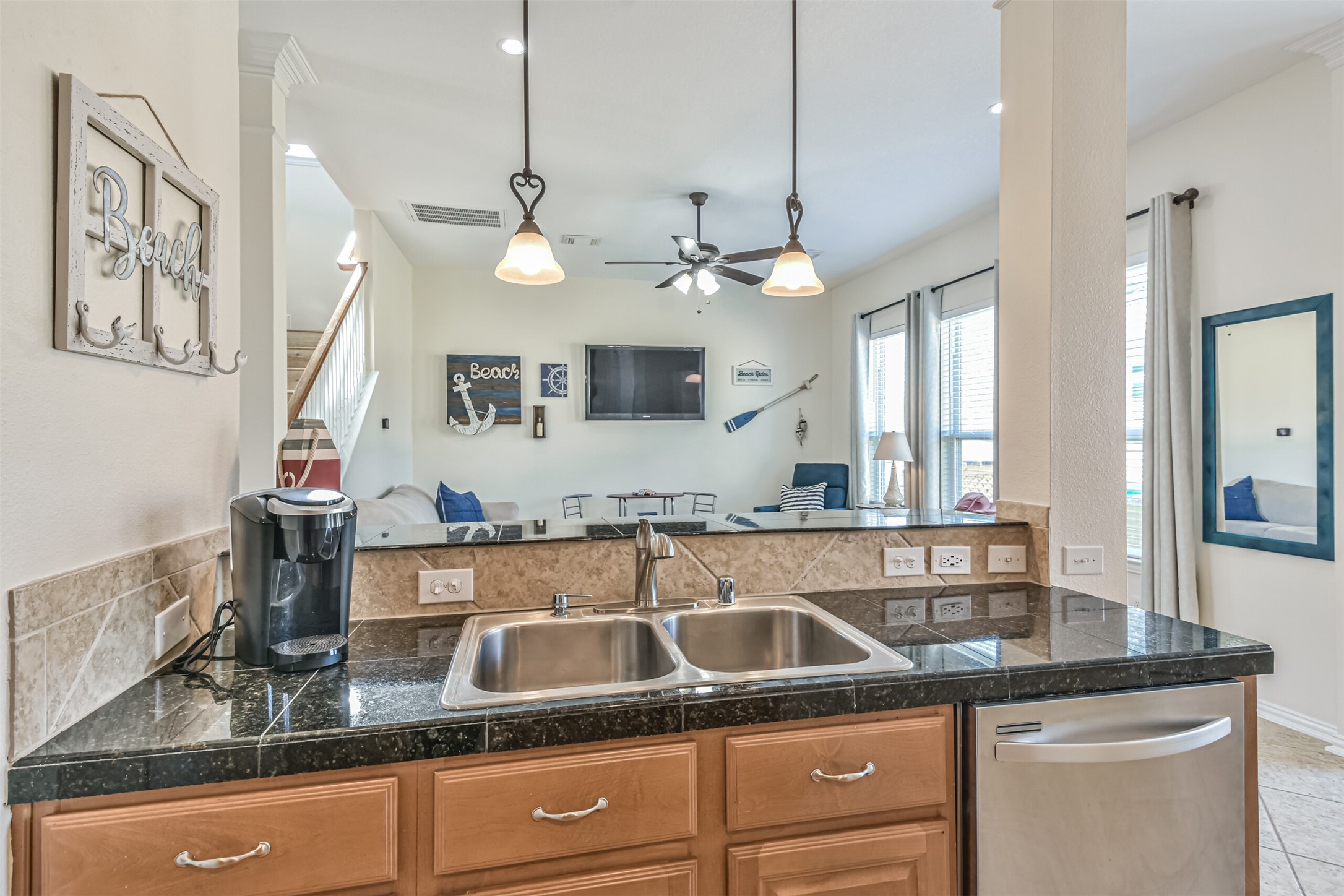 1815 28th Street Galveston, TX 77550 - Photo 29 of 42 This photo showcases a bright, open-concept kitchen and living area. The kitchen features granite countertops, a double sink, and stainless steel appliances. The living space has large windows, ample natural light, and beach-themed decor, creating a cozy and inviting atmosphere.