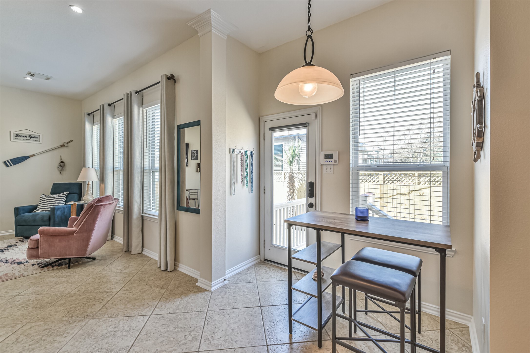 1815 28th Street Galveston, TX 77550 - Photo 30 of 42 This bright, airy space features large windows with blinds, a small dining area with bar stools, and a cozy sitting nook. The neutral tile flooring complements the light walls, creating a welcoming atmosphere ideal for relaxation and entertaining.