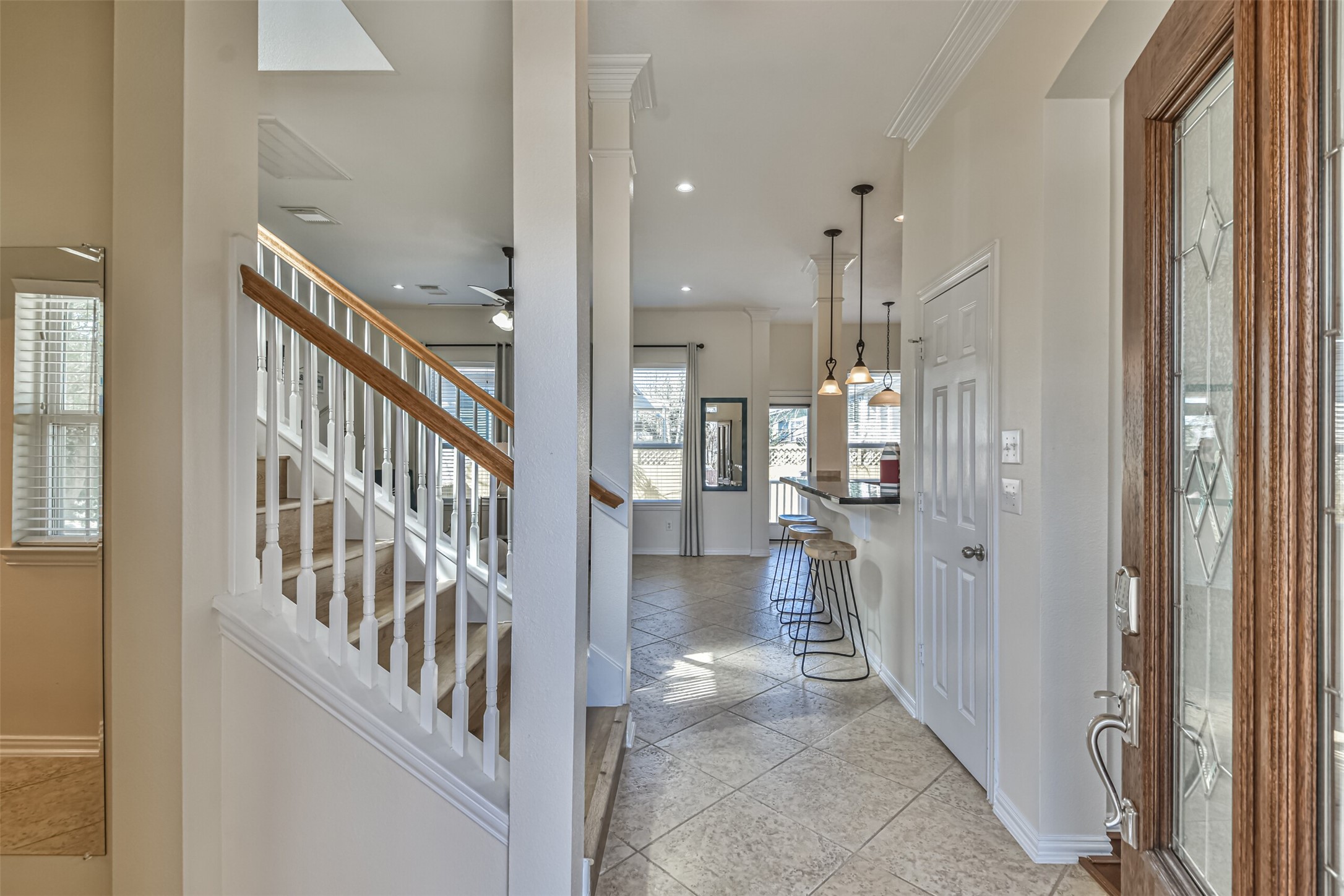 1815 28th Street Galveston, TX 77550 - Photo 3 of 42 Bright and welcoming entryway with tiled floors and a wooden staircase. The open layout leads to a modern kitchen with an island and bar stools, accented by pendant lighting.