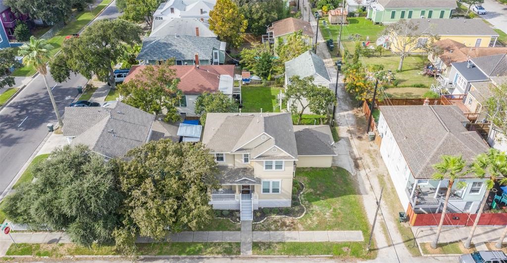 1815 28th Street Galveston, TX 77550 - Photo 40 of 42 This aerial photo shows a quaint neighborhood featuring a two-story house with a light exterior. The property has a small front yard with mature trees and a driveway. It's situated on a quiet street with similar charming homes nearby, offering a cozy community feel.