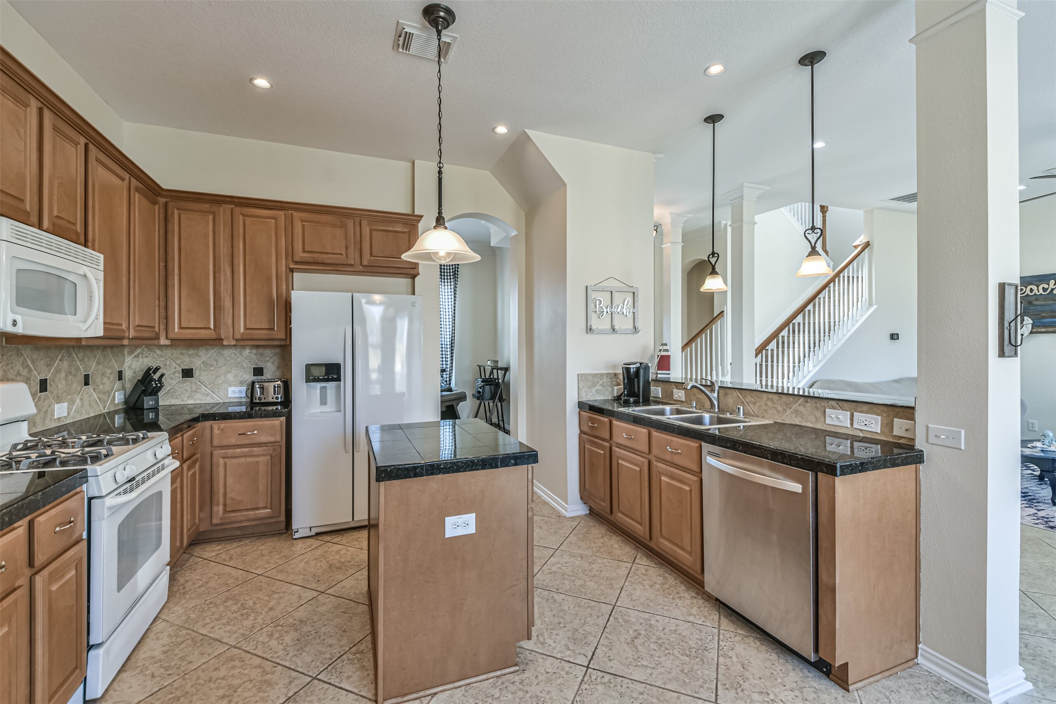 1815 28th Street Galveston, TX 77550 - Photo 6 of 42 This kitchen features elegant wood cabinetry, granite countertops, and modern appliances including a gas stove and double sink. The open layout includes a central island, tile flooring, and pendant lighting. Great flow to the adjacent living area and staircase.