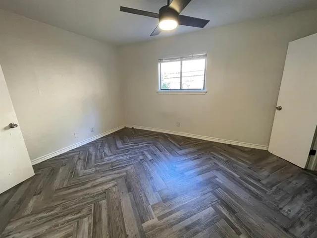 an empty room with wooden floor fan and windows