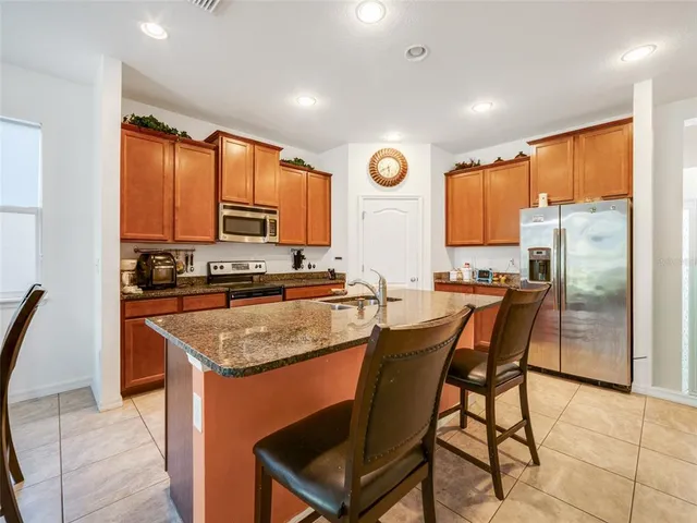 a kitchen with stainless steel appliances granite countertop a stove top oven a sink a refrigerator with a dining table and chairs with wooden floor