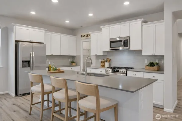 a kitchen with stainless steel appliances granite countertop a stove a sink a microwave a refrigerator and white cabinets