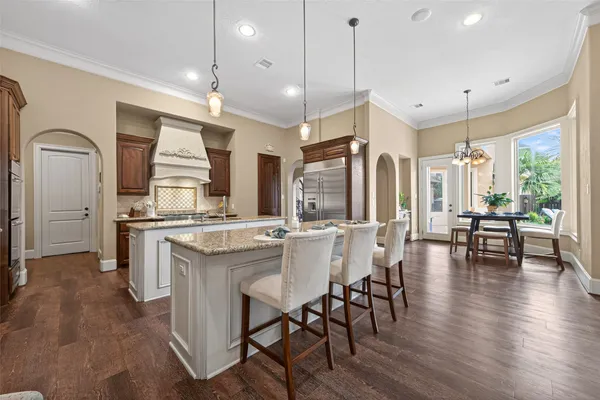 a kitchen with kitchen island granite countertop a table chairs stove a sink dishwasher and cabinets with wooden floor
