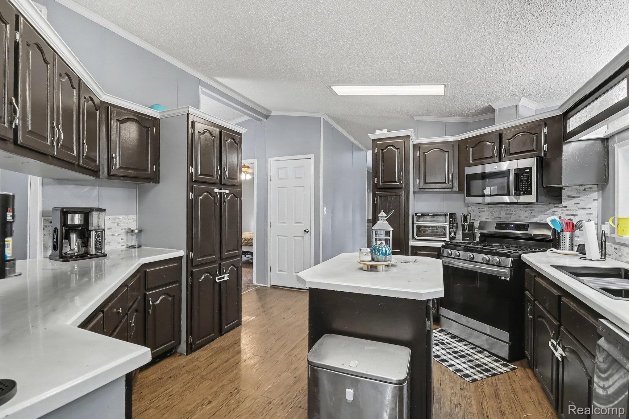 6357 North State Road Davison, MI 48423 - Photo 12 of 33 Spacious kitchen featuring dark cabinetry, light countertops, wood-finish flooring, a central island, and stainless steel appliances