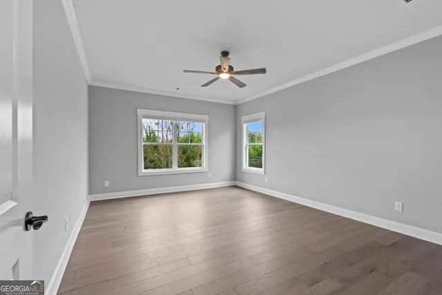 an empty room with wooden floor ceiling fan and windows