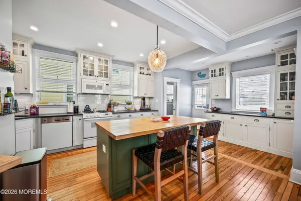 a kitchen with stainless steel appliances granite countertop a stove top oven a sink dishwasher and white cabinets with wooden floor