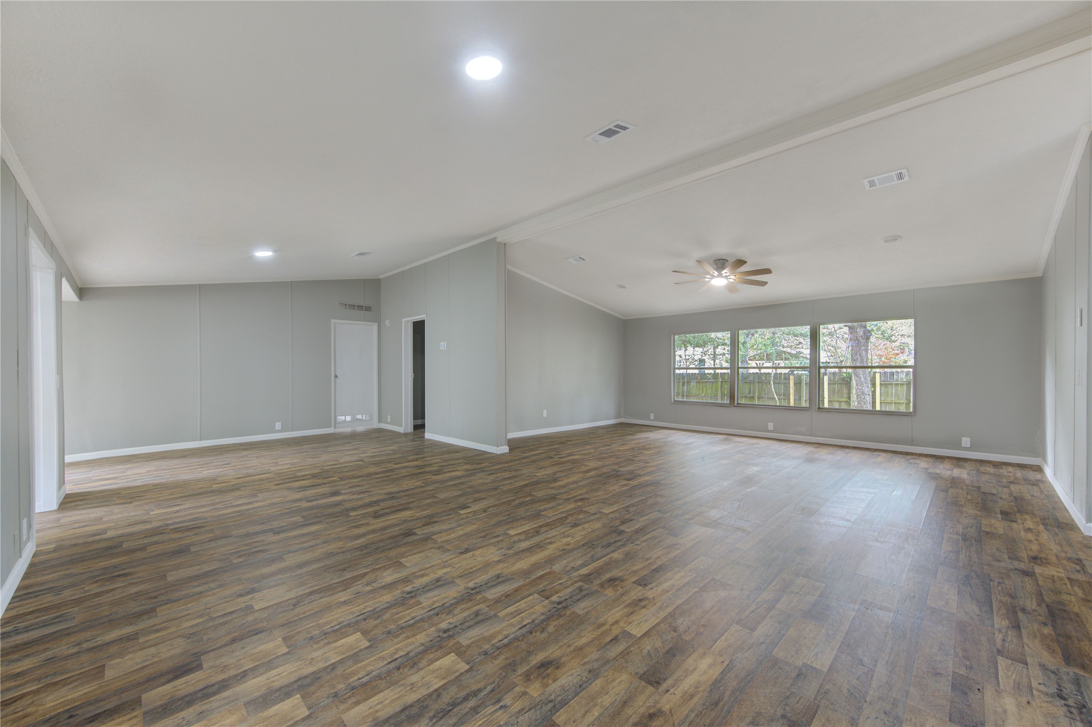 30226 Davis Street Magnolia, TX 77355 - Photo 7 of 50 This photo showcases a spacious, open living area with light gray walls and warm wood flooring. Large windows provide ample natural light, and a ceiling fan adds functionality and style.