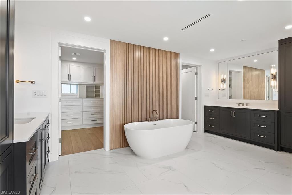 13935 Old Coast Road, Unit 2206 Naples, FL 34110 - Photo 11 of 50 Spa-style bath featuring a soaking tub, his-and-hers storage, and a striking warm wood accent wall