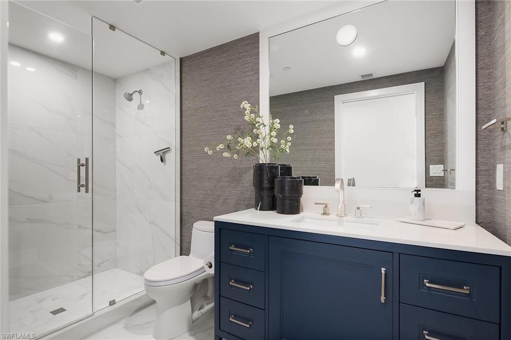 13935 Old Coast Road, Unit 2206 Naples, FL 34110 - Photo 25 of 50 Third guest en-suite bath featuring a glass walk-in shower, quartz surfaces, custom cabinetry, and designer wallpaper.