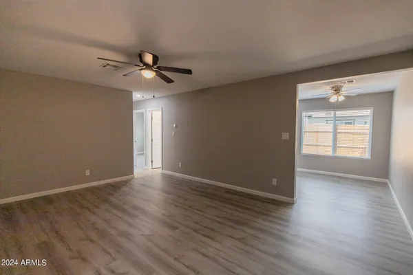 an empty room with wooden floor ceiling fan and windows