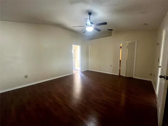a view of an empty room with wooden floor and a ceiling fan