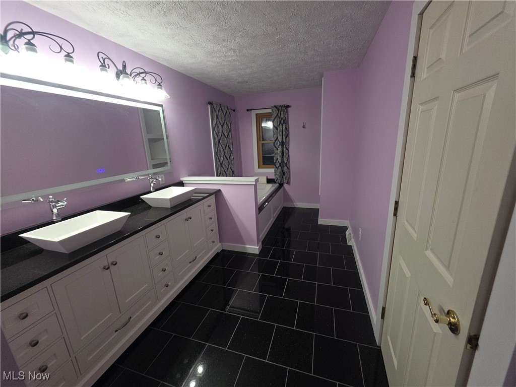 2291 Armstrong Road Wooster, OH 44691 - Photo 12 of 23 Newly updated master bathroom with double vanity, a soaking tub, a textured ceiling, and dark tile patterned floors