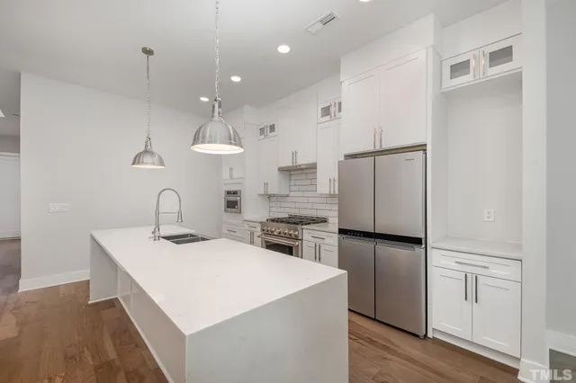 a kitchen with kitchen island a counter top space a sink a refrigerator and white cabinets